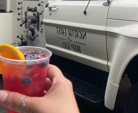 Hand holds a drink in front of the North East Tap Company Beer Truck.